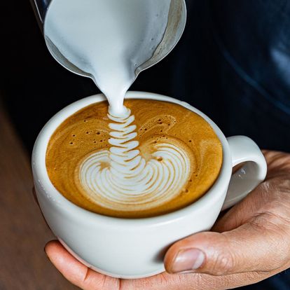 a hand doing latte art in a cup of coffee 